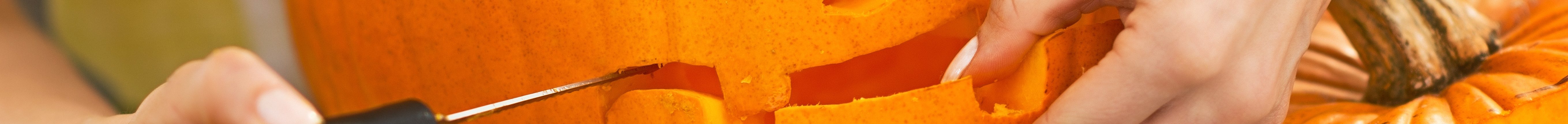 Closeup on housewife carving a big orange pumpkin Jack-O-Lantern